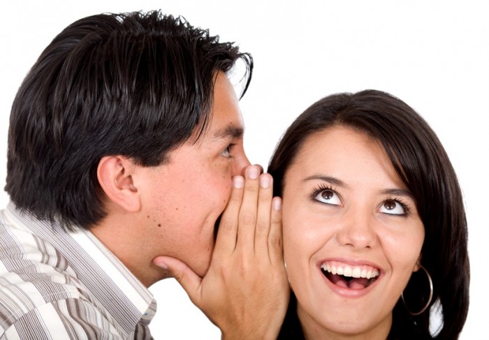 man telling a secret to a girl - she is looking surprised over a white background