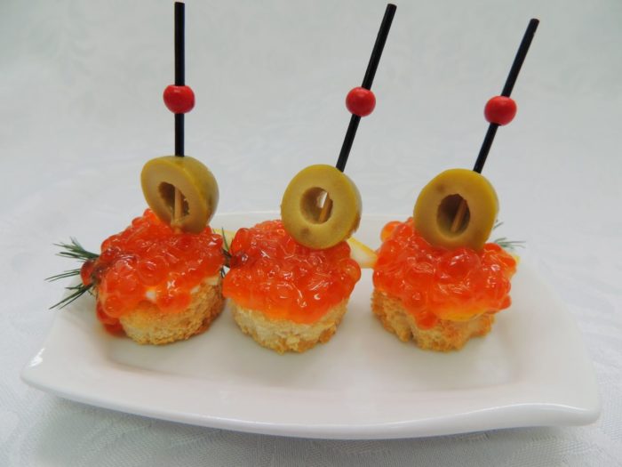 Canape for a buffet with red caviar, olives and greens