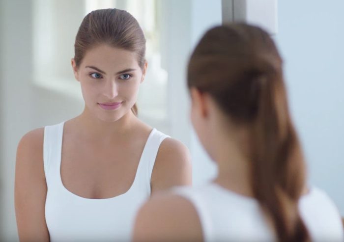 девушка смотриться в зеркало после нескольких процедур пилинга кожи лица и головы