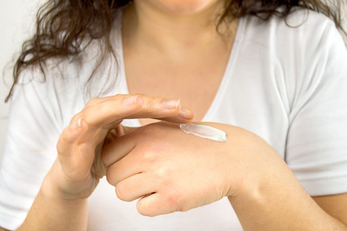 девушка наносит на руку крем-эмолент для увлажнения кожи из-за атопического дерматита