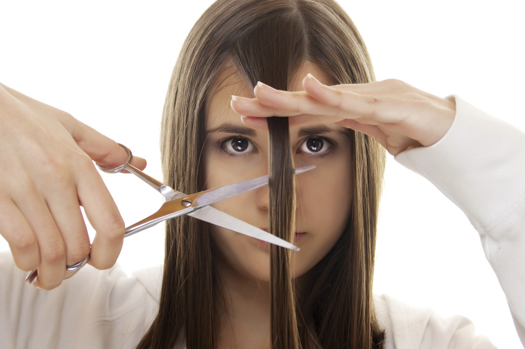 Teenage girl cutting her hair with scissors