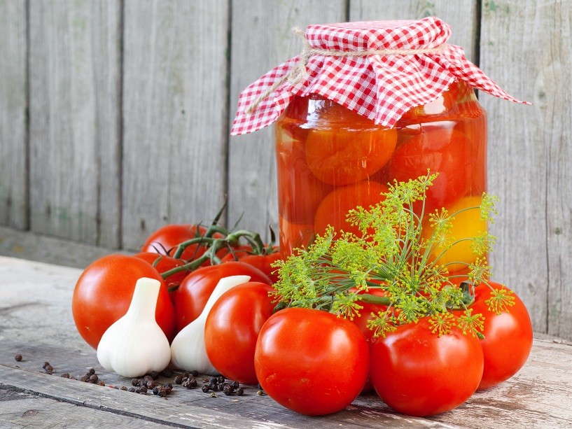 Homemade tomatoes in glass jar. Fresh and canned tomatoes on woo