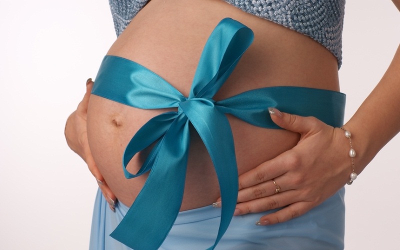 Живот беременной женщины, перевязанный синей подарочной лентой